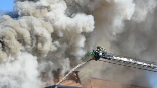 Brandweerman blust een dakbrand vanuit een hoogwerker