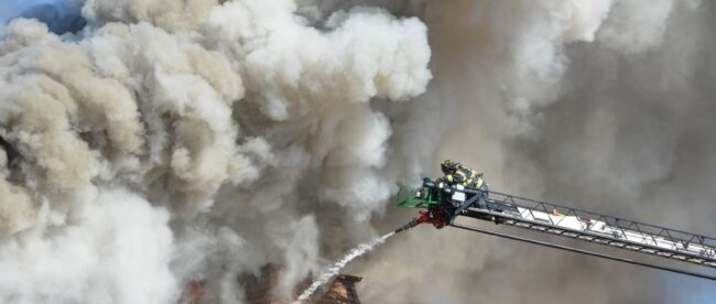 Brandweerman blust een dakbrand vanuit een hoogwerker