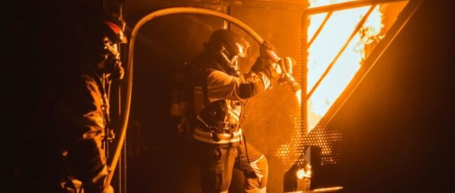 Brandweerlieden bestrijden een felle brand in een metalen ruimte