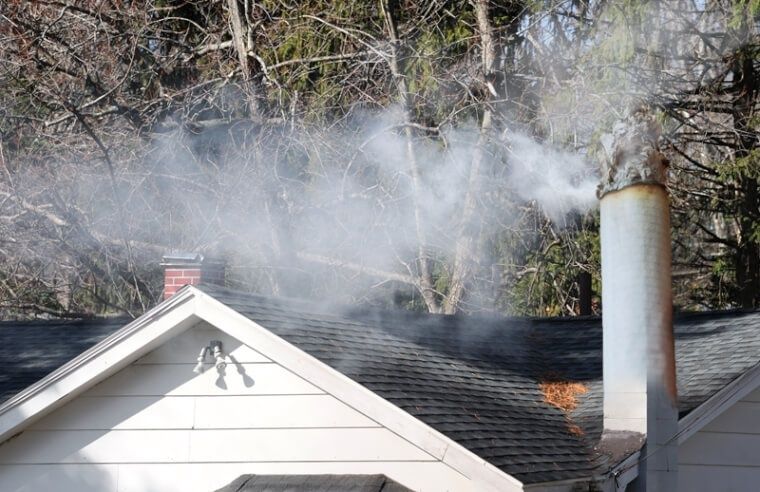 Rook kringelt uit een schoorsteen boven een woning tussen de bomen